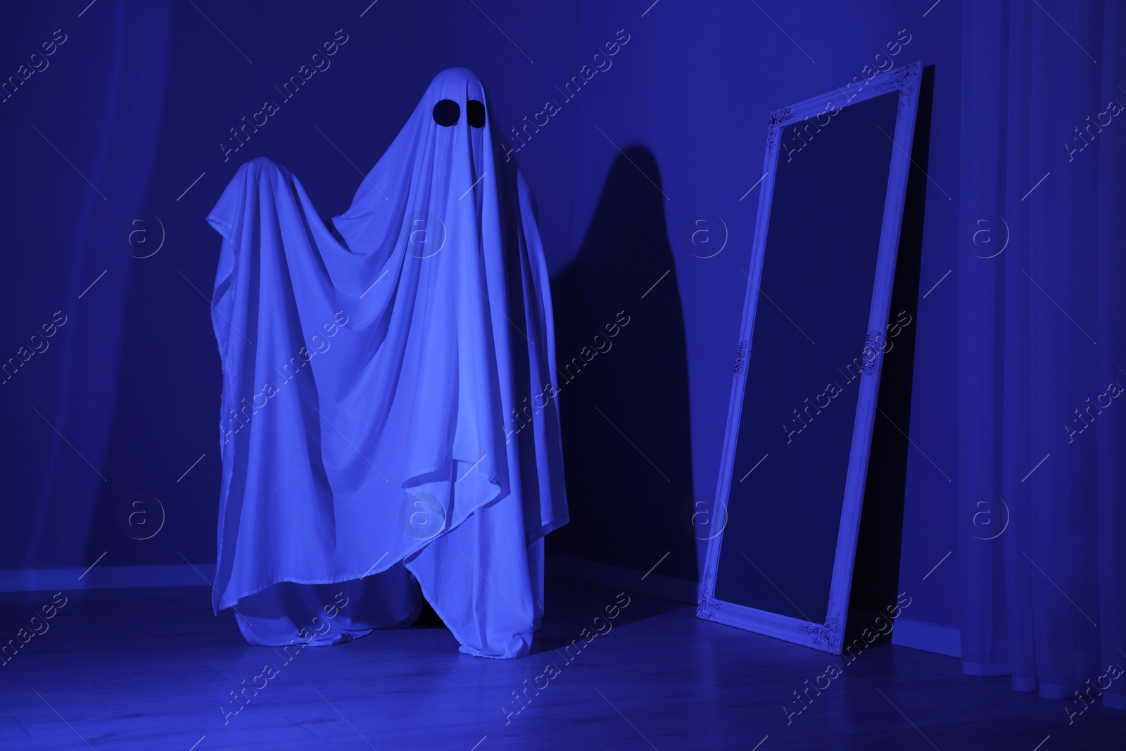 Photo of Creepy ghost. Woman covered with sheet in blue light