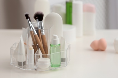 Organizer with cosmetic products and makeup accessories on table against blurred background. Space for text