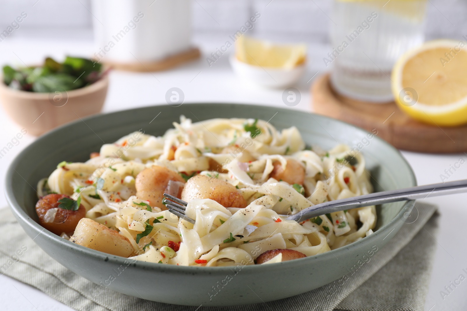 Photo of Delicious scallop pasta with spices in bowl served on light table, closeup