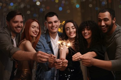 Photo of Happy friends with sparklers celebrating birthday indoors