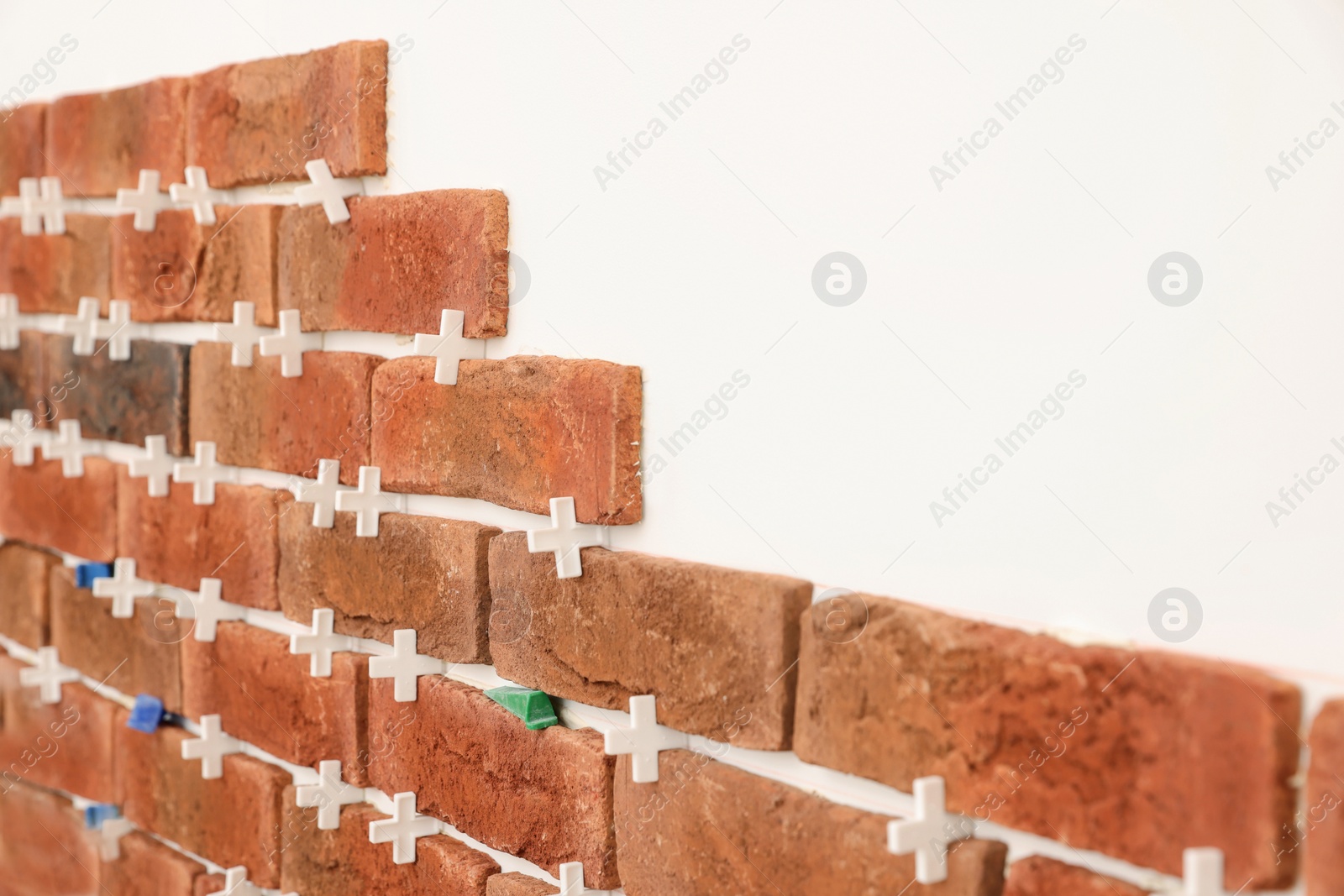 Photo of Decorative bricks with tile leveling system on white wall in room