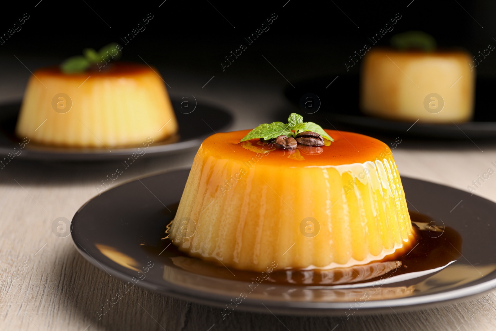Photo of Plate of delicious caramel pudding with coffee beans and mint on white wooden table, closeup