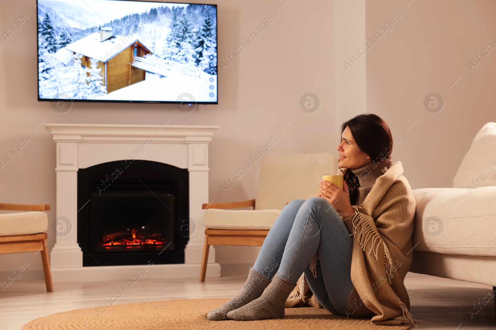 Photo of Young woman with cup of tea relaxing on floor near fireplace at home