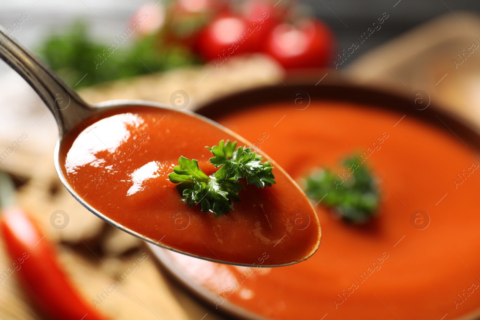 Photo of Spoon with fresh homemade tomato soup on blurred background, closeup. Space for text