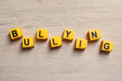 Photo of Word Bullying made of yellow cubes with letters on wooden table, flat lay