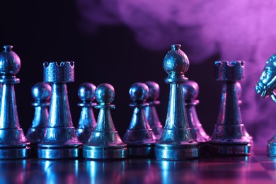 Chess pieces on board in color light, selective focus