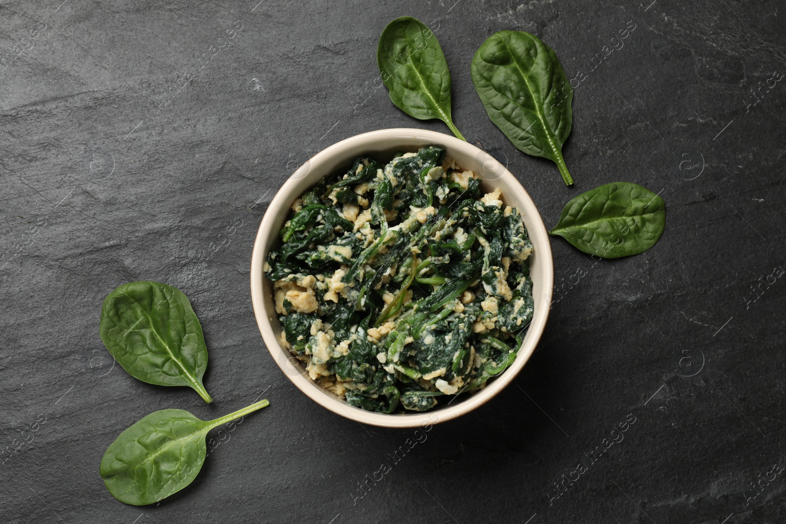 Photo of Tasty spinach dip with egg in bowl on black table, top view