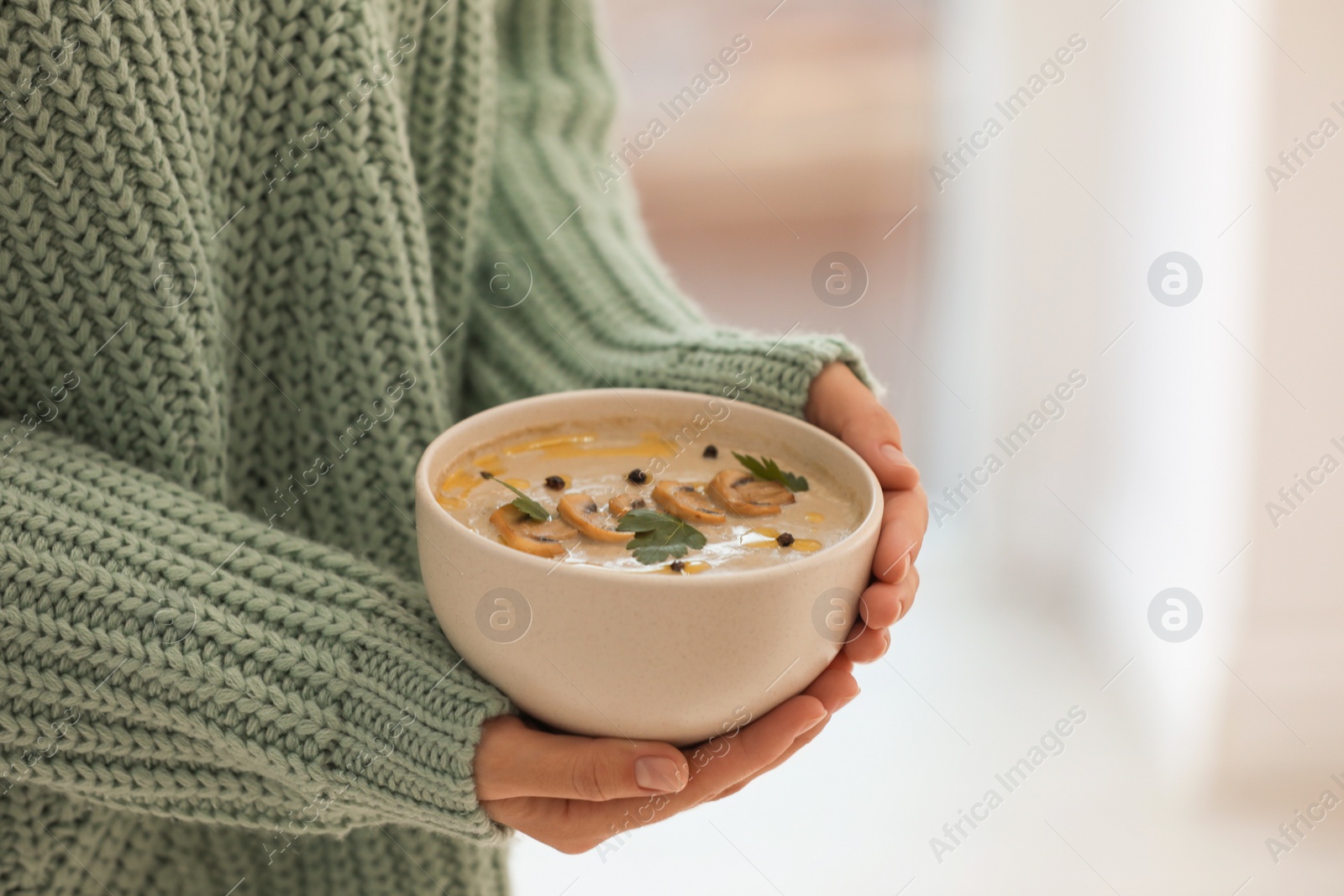 Photo of Young woman with bowl of cream soup on blurred background, closeup