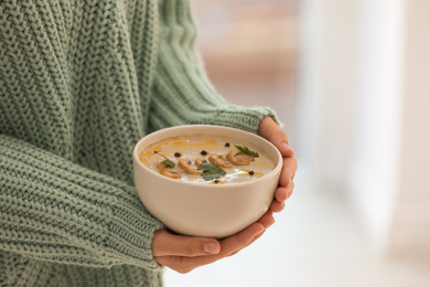 Young woman with bowl of cream soup on blurred background, closeup