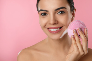 Photo of Young woman holding facial cleansing brush on pink background, closeup. Washing accessory