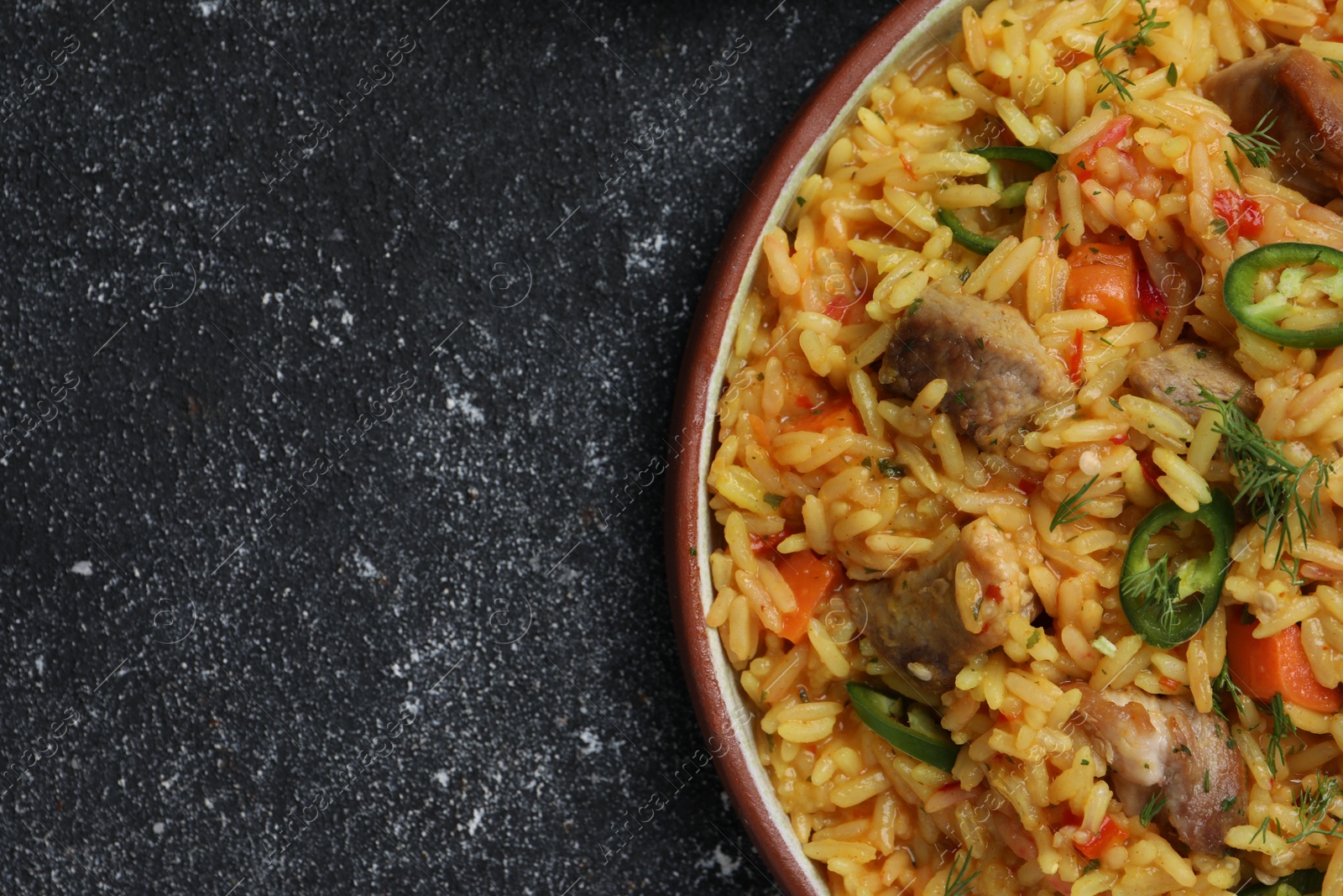 Photo of Delicious pilaf with meat on black textured table, top view. Space for text