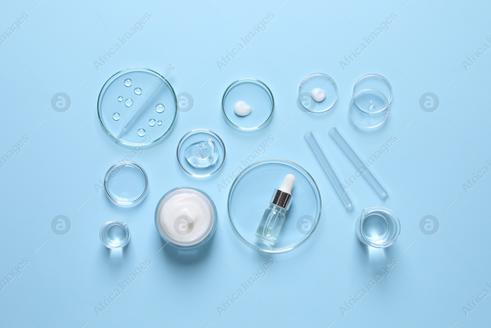 Photo of Laboratory glassware and natural ingredients for organic cosmetic product on light blue background, flat lay