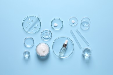 Photo of Laboratory glassware and natural ingredients for organic cosmetic product on light blue background, flat lay