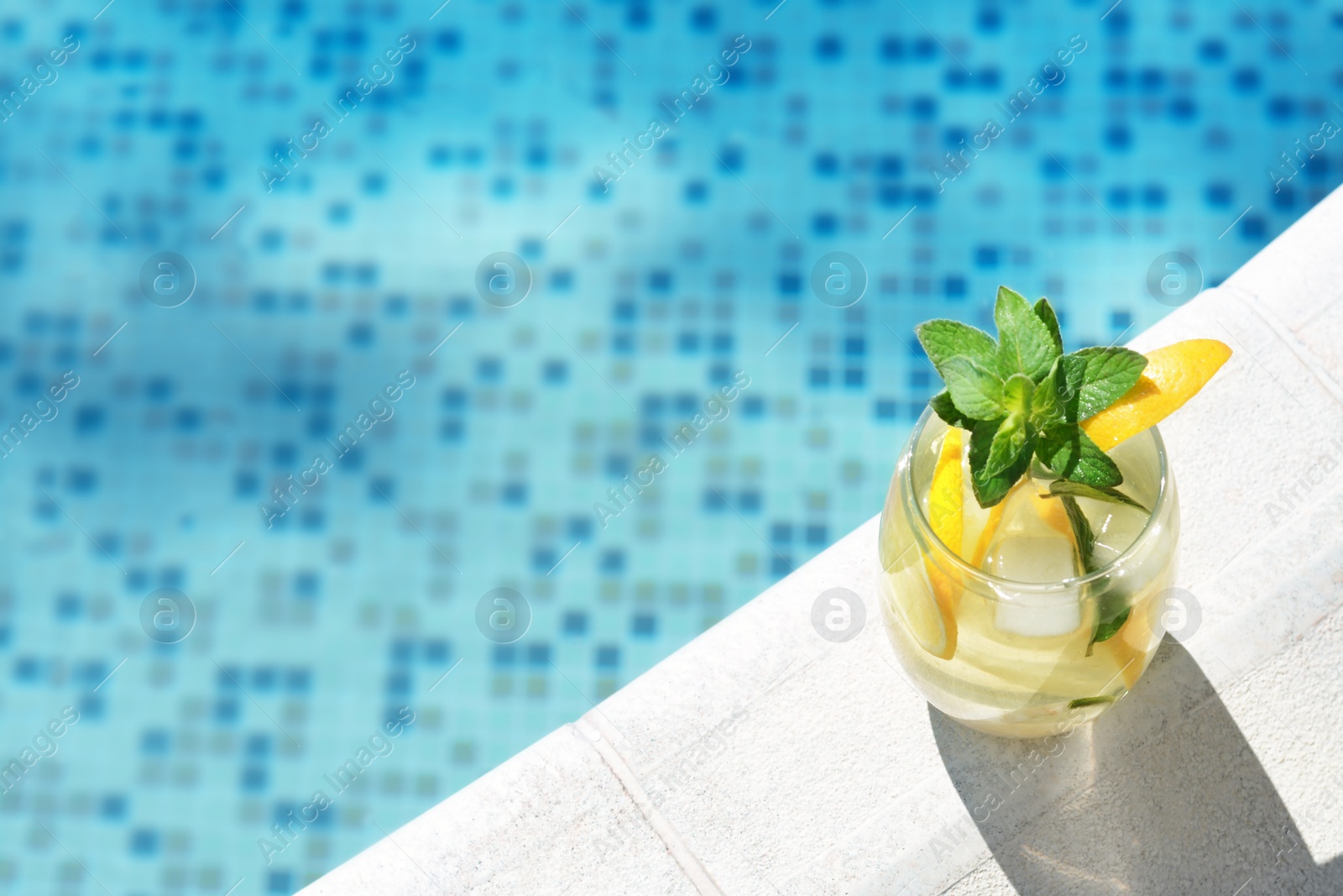 Photo of Refreshing water with lemon slices and mint near swimming pool. Space for text