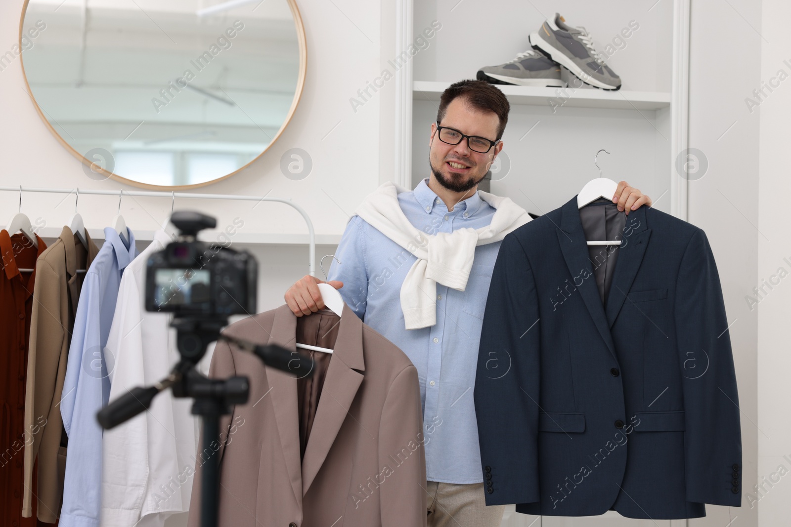 Photo of Smiling fashion blogger showing clothes while recording video at home