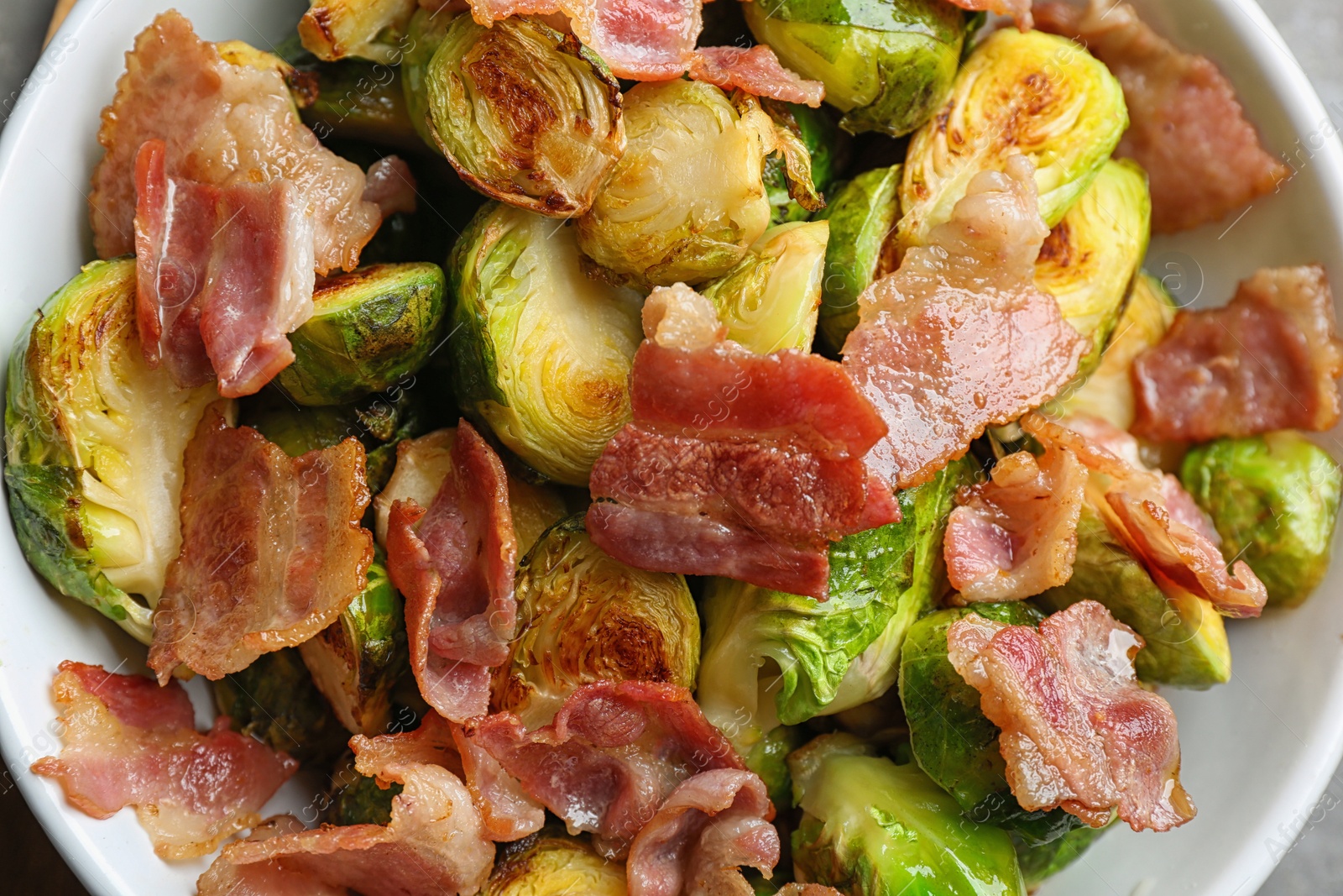 Photo of Delicious roasted Brussels sprouts with bacon in bowl, top view