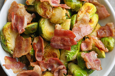 Photo of Delicious roasted Brussels sprouts with bacon in bowl, top view