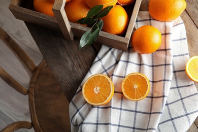 Fresh oranges with leaves and rustic box on wooden table, above view