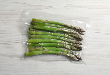Photo of Asparagus in vacuum pack on white wooden table, top view