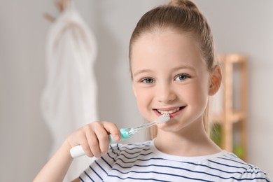 Cute little girl brushing her teeth with electric toothbrush in bathroom