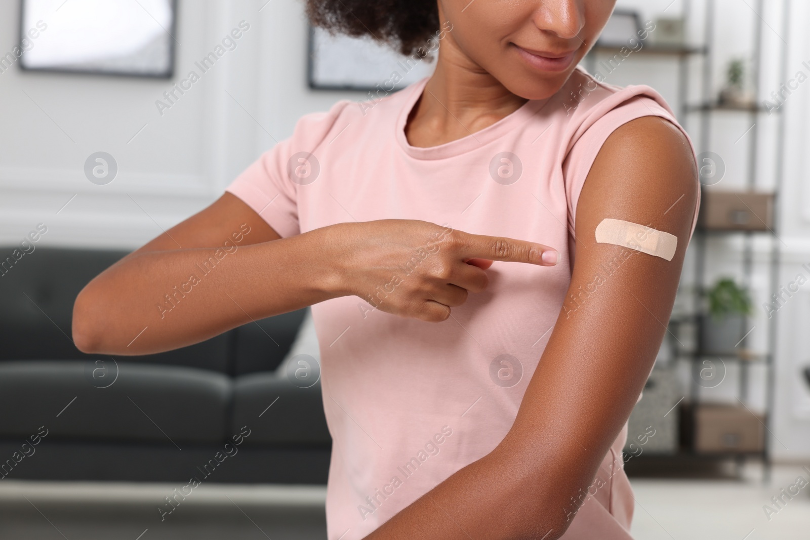 Photo of Young woman pointing at adhesive bandage after vaccination indoors, closeup