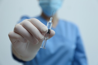 Photo of Doctor holding syringe with COVID-19 vaccine on light background, closeup