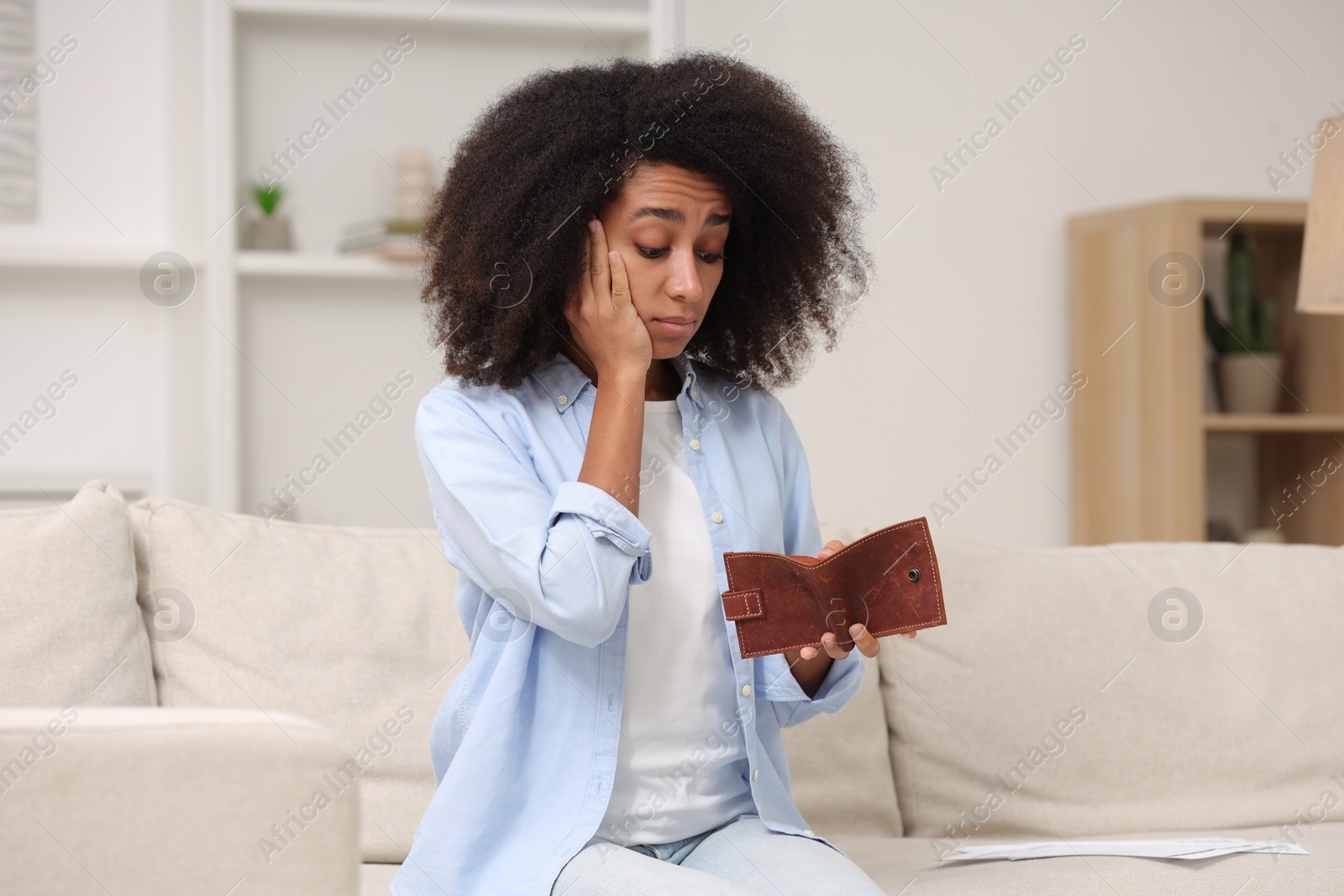 Photo of Shocked woman with empty wallet at home. Debt problem