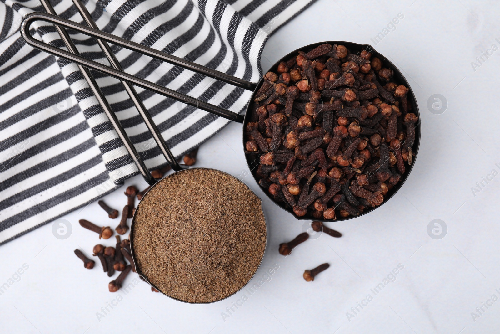 Photo of Aromatic clove powder and dried buds in scoops on white table, top view