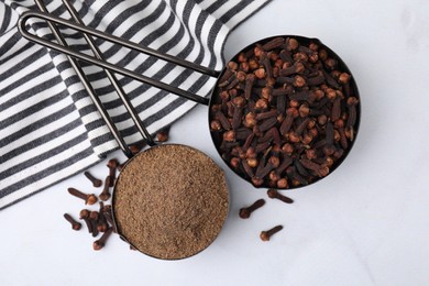 Aromatic clove powder and dried buds in scoops on white table, top view