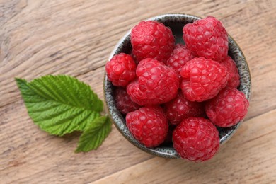 Photo of Tasty ripe raspberries and green leaves on wooden table, top view
