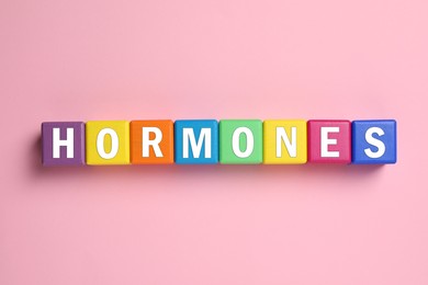 Word Hormones made of colorful cubes with letters on pink background, flat lay
