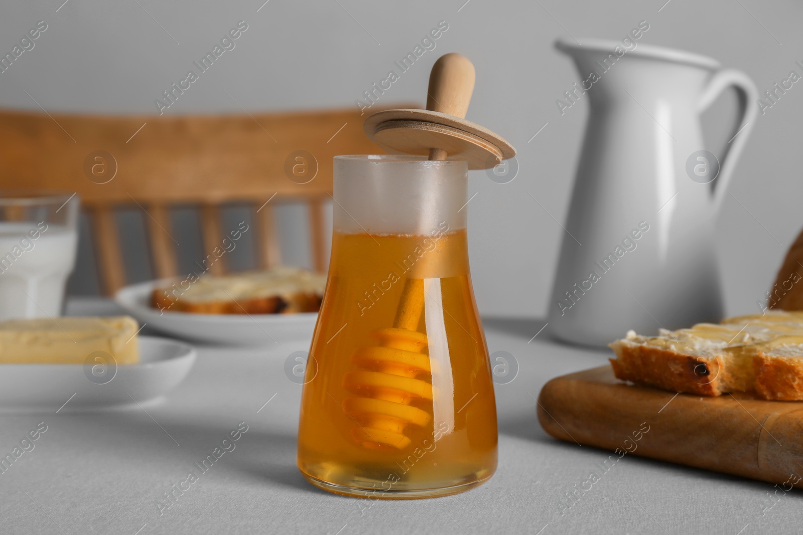 Photo of Jar of tasty honey, milk and bread with butter on white table