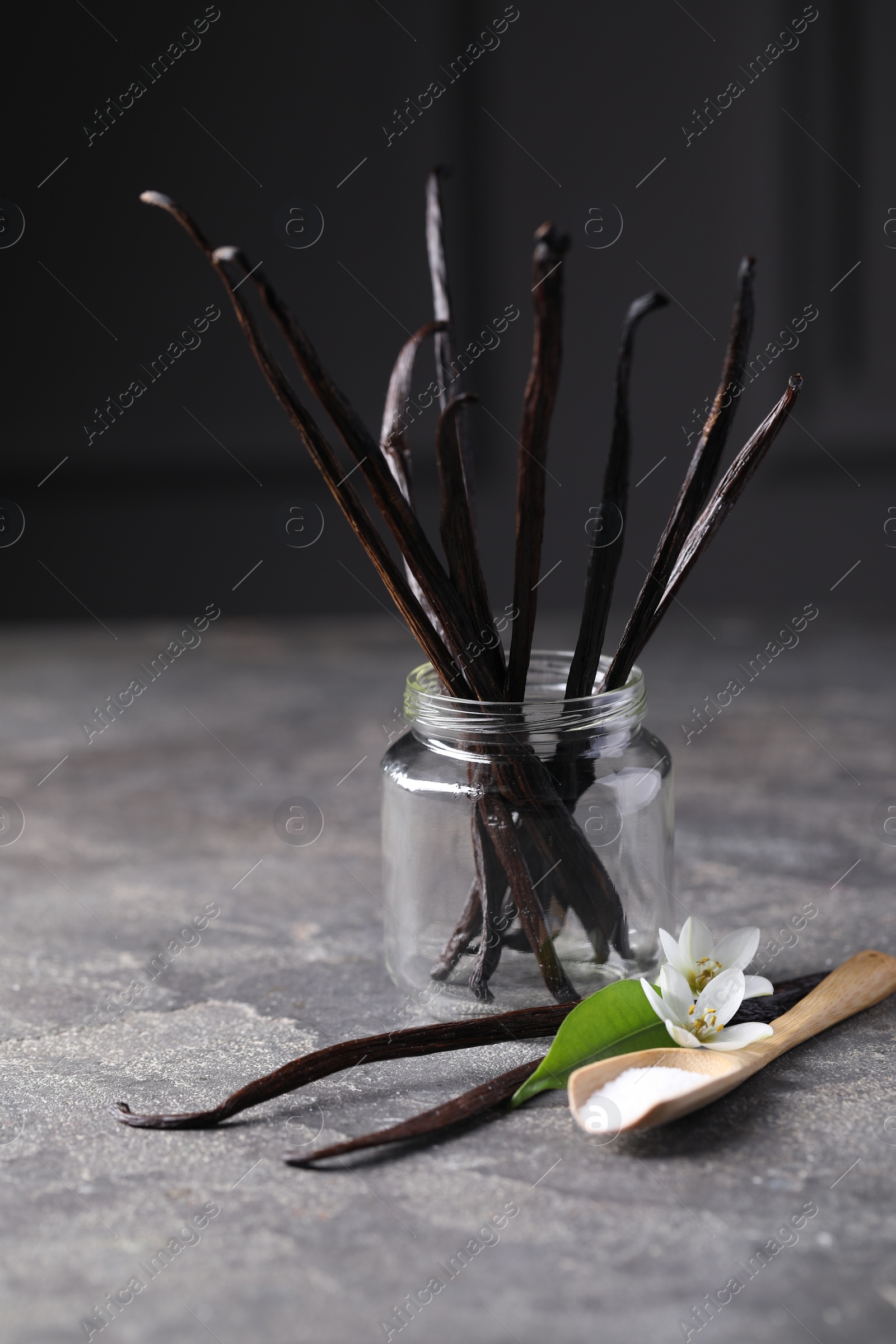 Photo of Spoon with sugar, flowers, leaf and vanilla pods on grey textured table