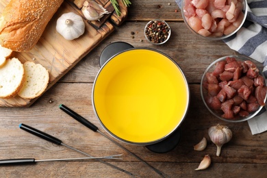 Flat lay composition with oil pot and meat fondue ingredients on wooden background