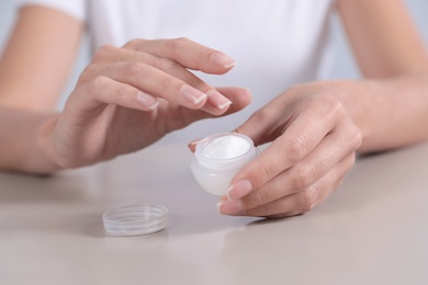 Photo of Young woman holding jar of cream at table, closeup