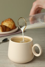 Photo of Woman pouring milk into cup of coffee at wooden table, closeup