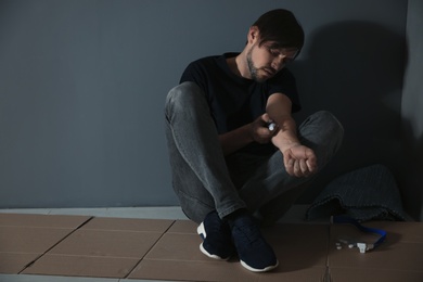 Photo of Male drug addict making injection near grey wall. Space for text