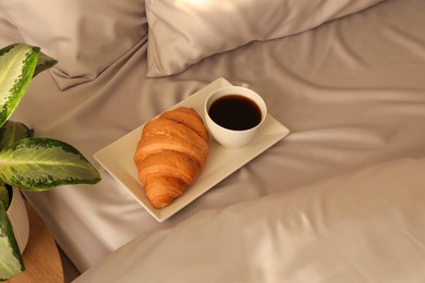 Photo of Tasty croissant and aromatic coffee on bed with stylish silky linens