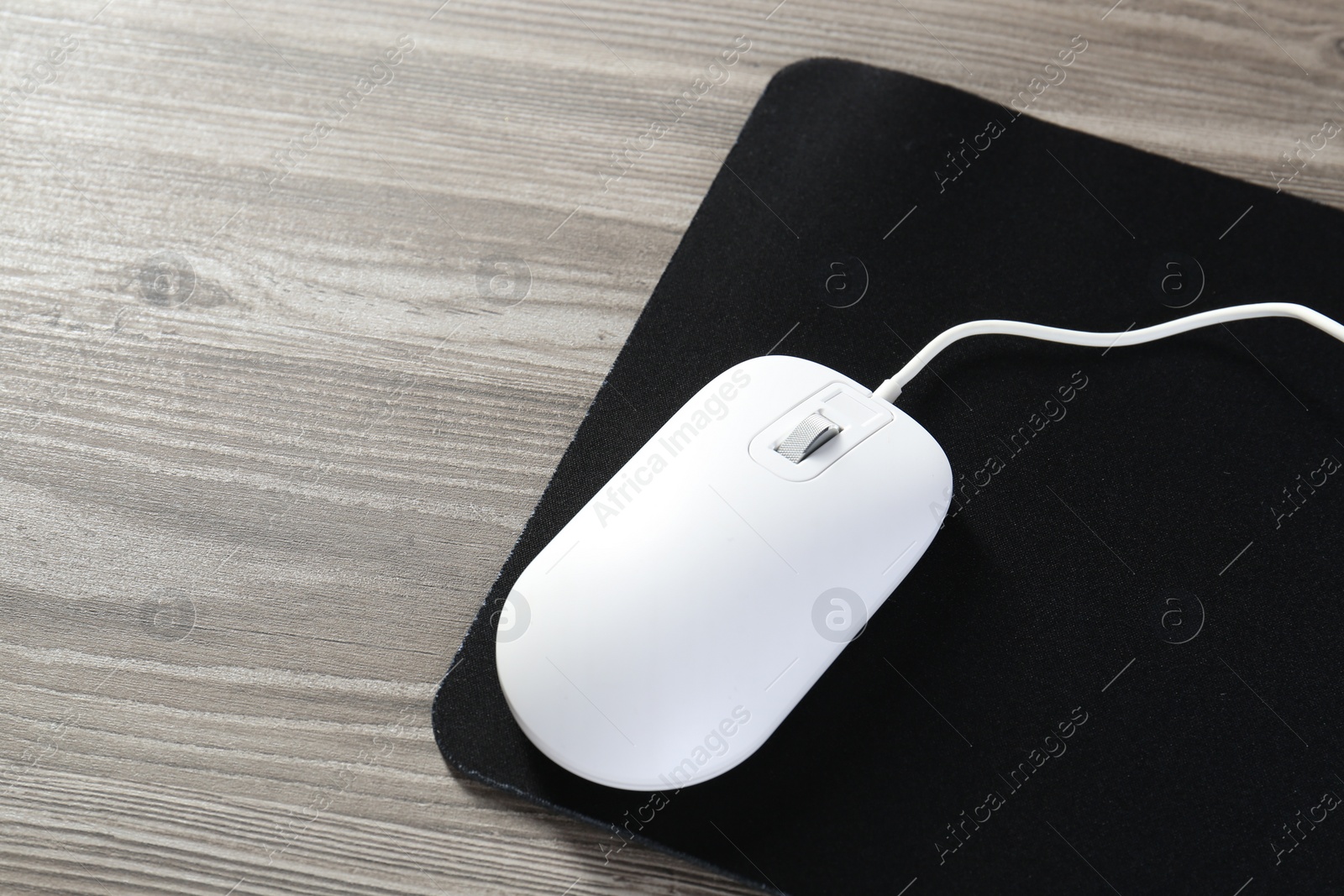 Photo of Wired mouse and mousepad on wooden table, space for text