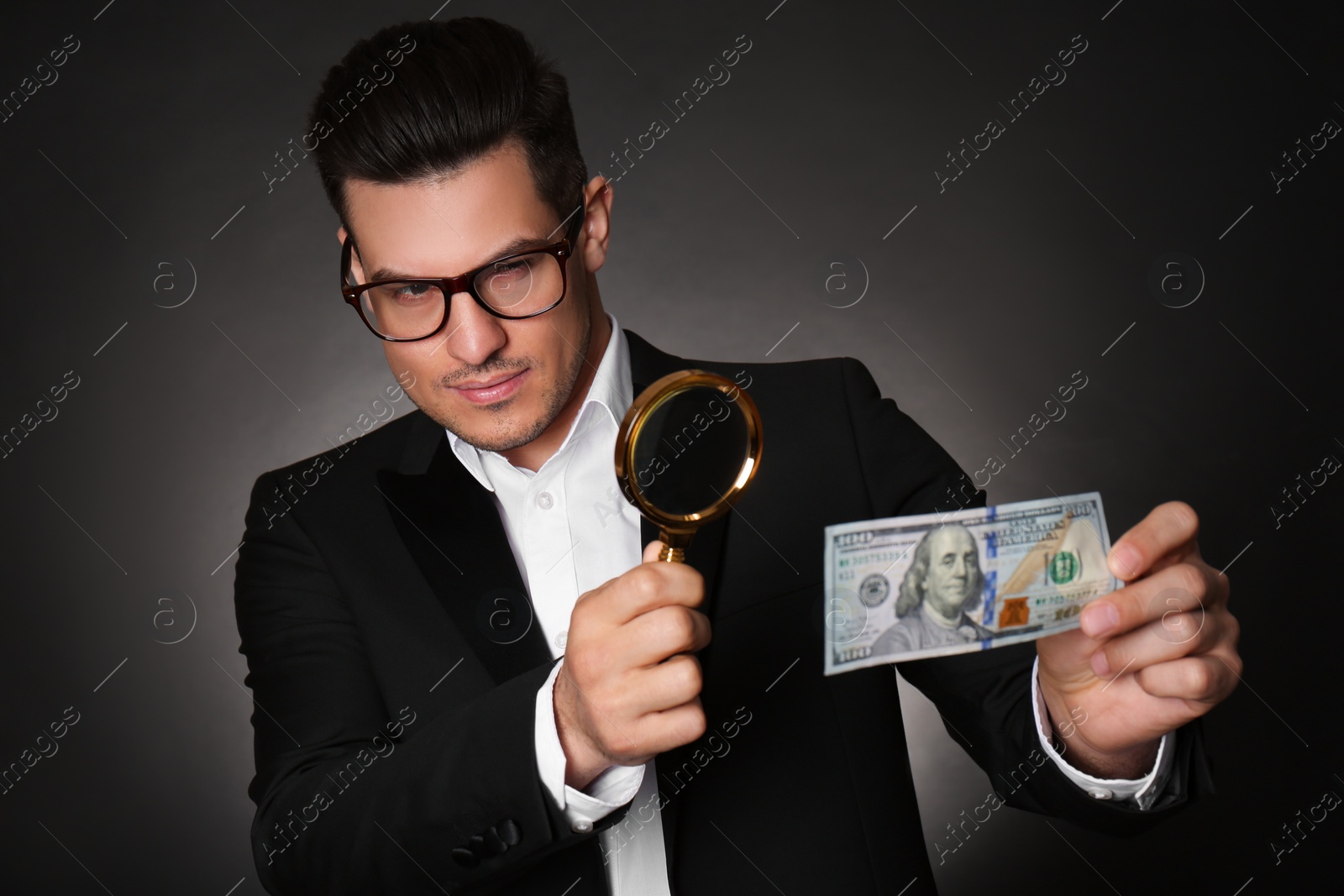 Photo of Expert authenticating 100 dollar banknote with magnifying glass against dark background. Fake money concept