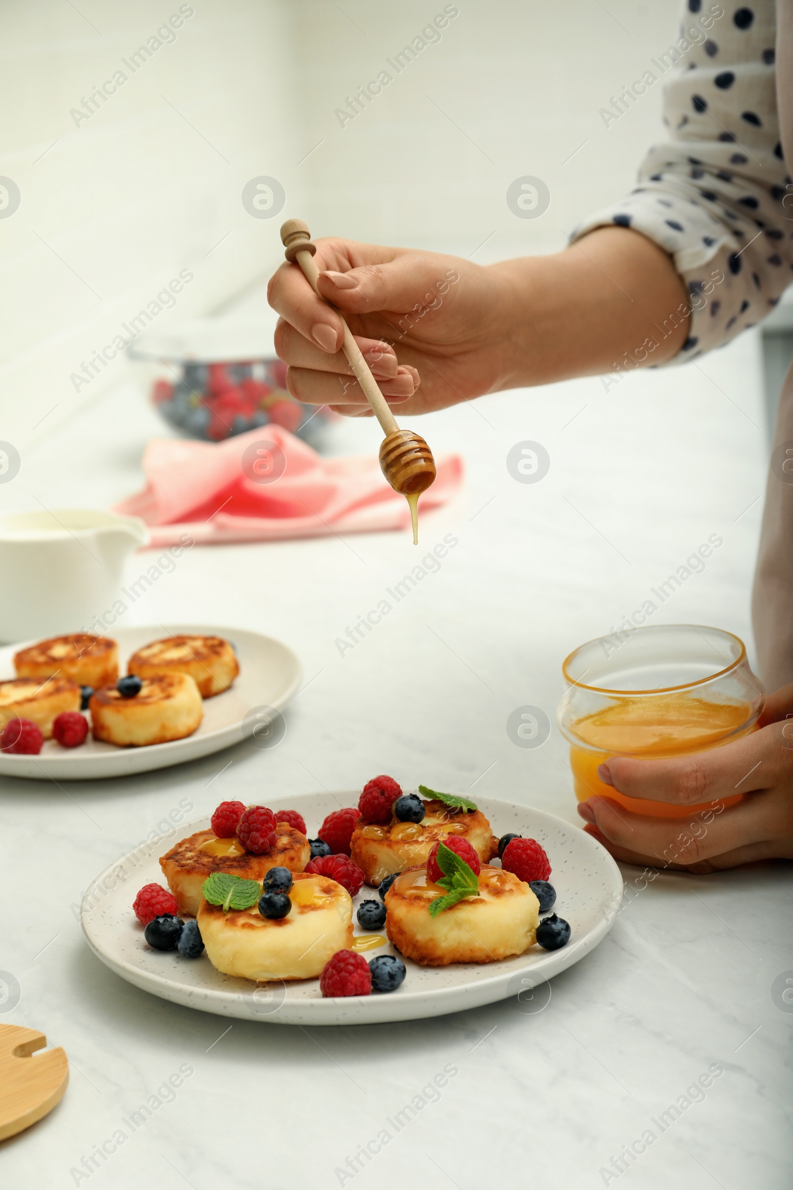 Photo of Woman pouring honey onto delicious cottage cheese pancakes at white table, closeup