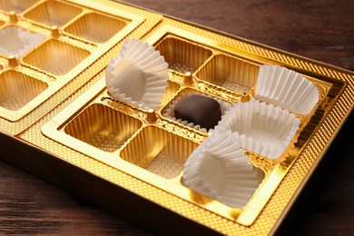 Photo of Partially empty box of chocolate candies on wooden table, closeup