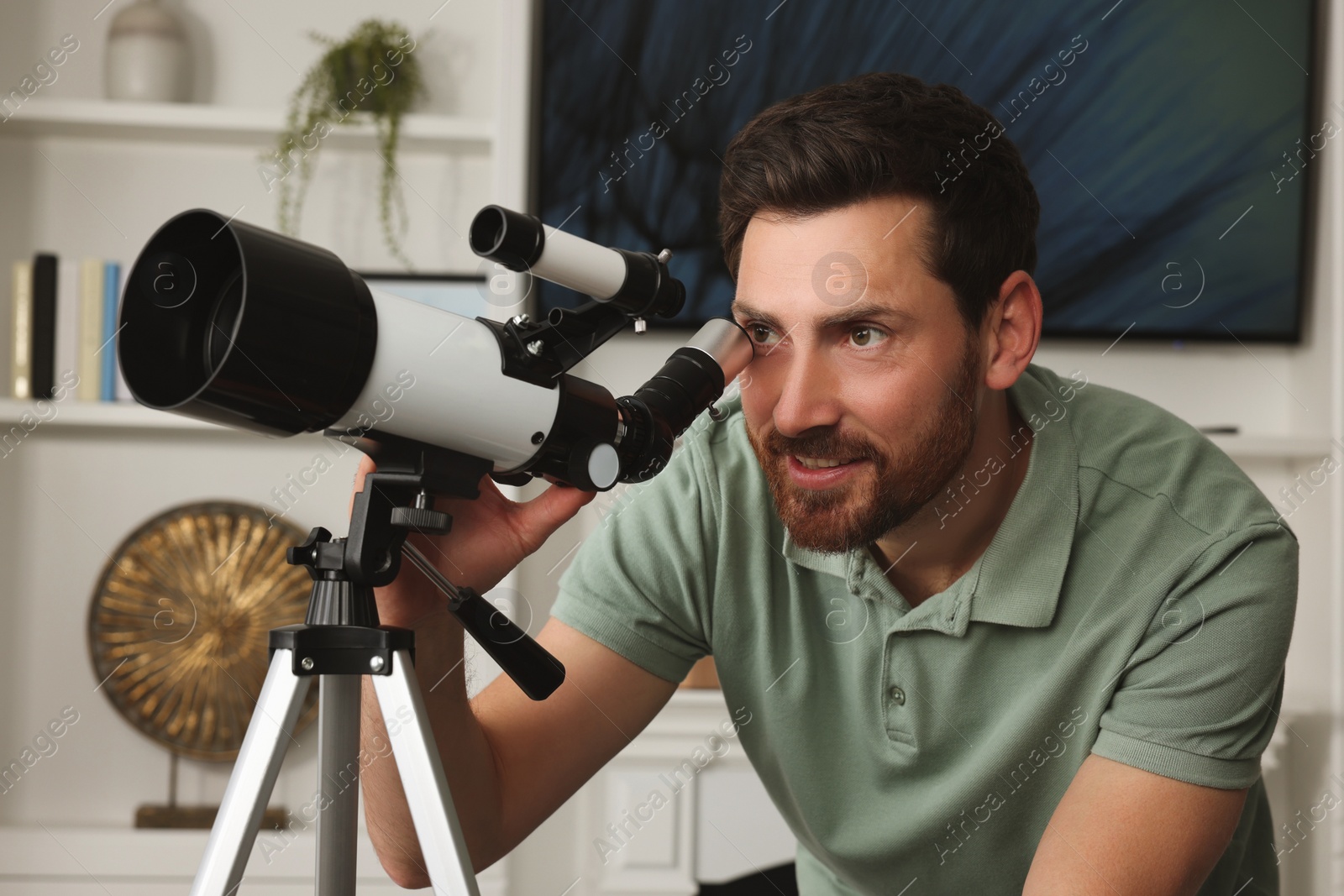 Photo of Handsome man using telescope to look at stars in room