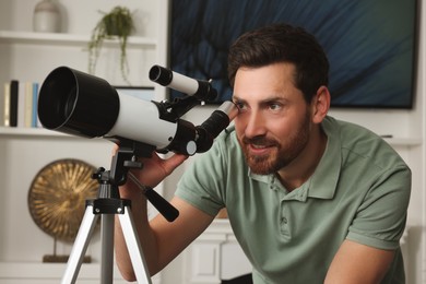 Handsome man using telescope to look at stars in room