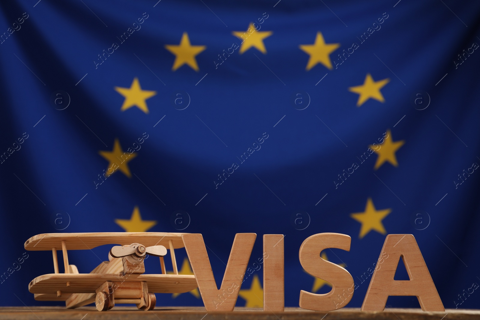 Photo of Word Visa made of wooden letters and toy plane on table against European Union flag. Space for text