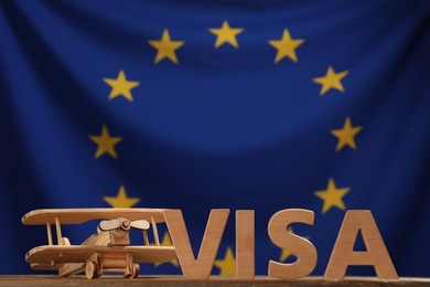 Word Visa made of wooden letters and toy plane on table against European Union flag. Space for text