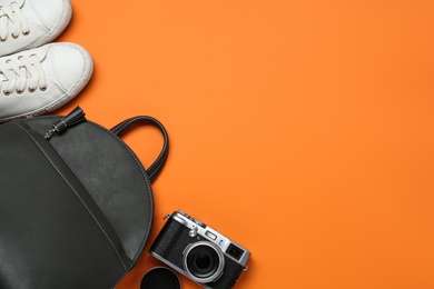 Photo of Grey backpack, sneakers and camera on orange background, flat lay. Space for text