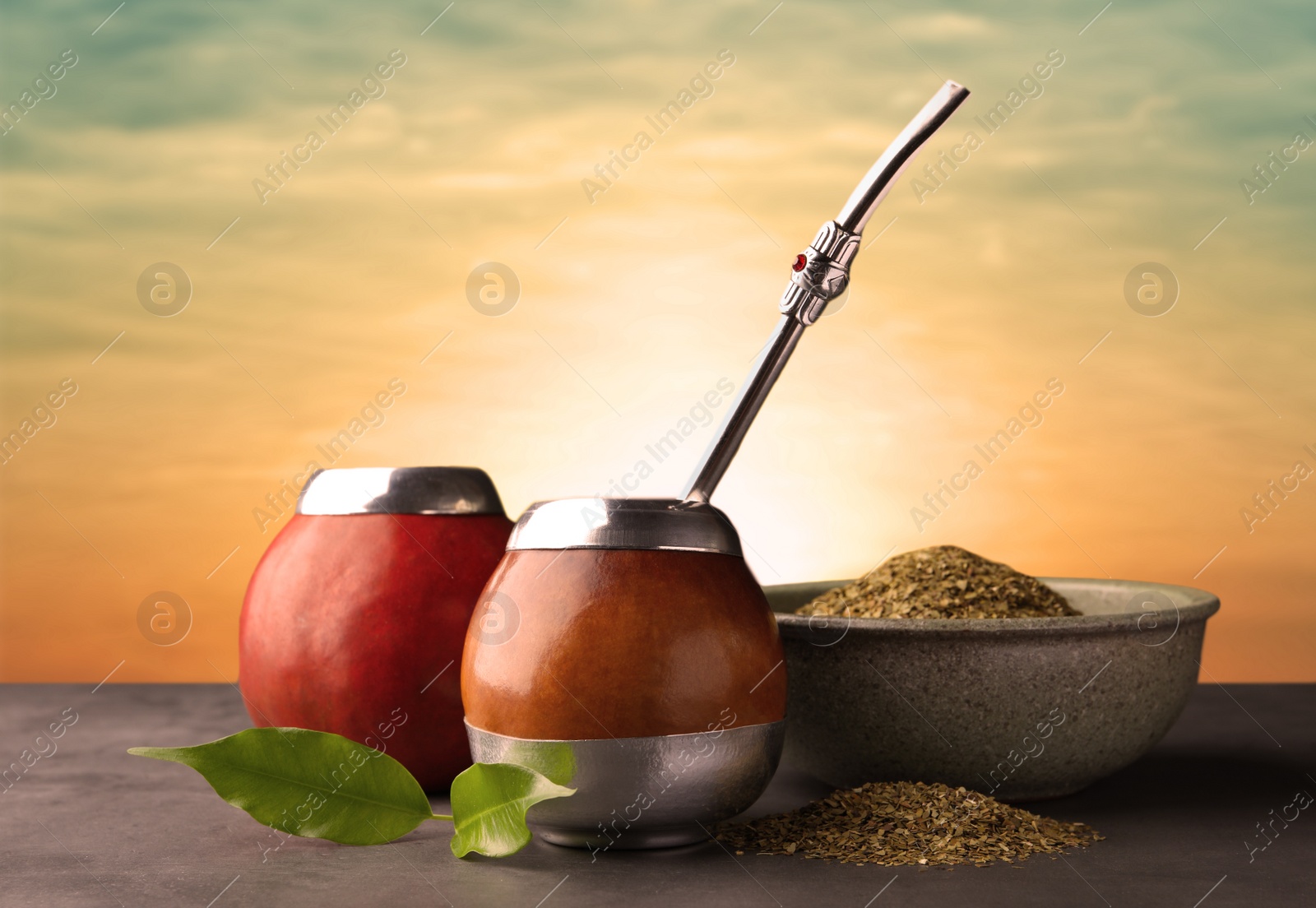 Image of Calabashes with mate tea and bombilla on light grey table outdoors at sunset