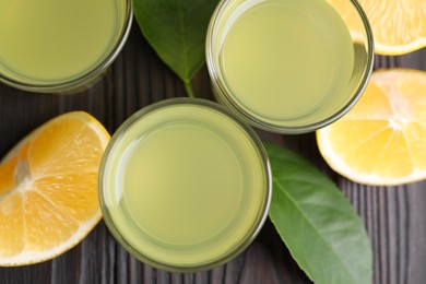 Photo of Tasty limoncello liqueur, lemon and green leaves on dark wooden table, flat lay