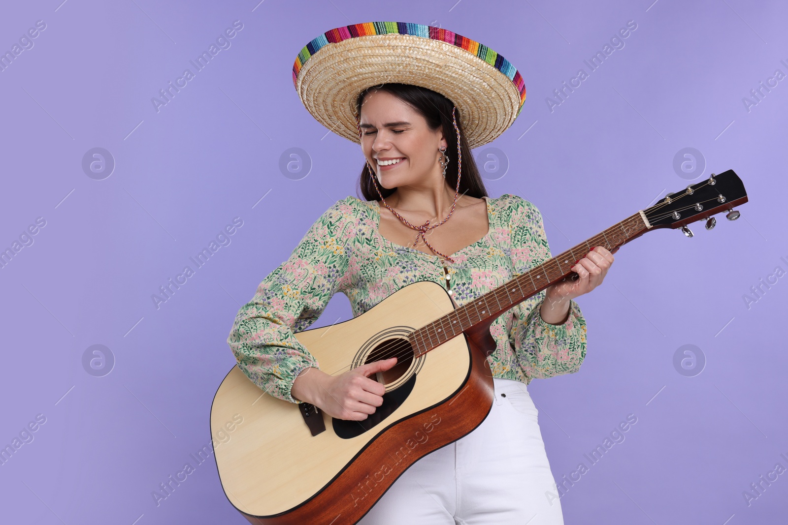 Photo of Young woman in Mexican sombrero hat playing guitar on violet background